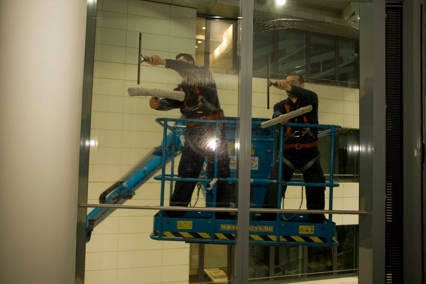 Laveurs de vitres Belux Cleaning sur une nacelle élévatrice nettoyant les vitres d'un building